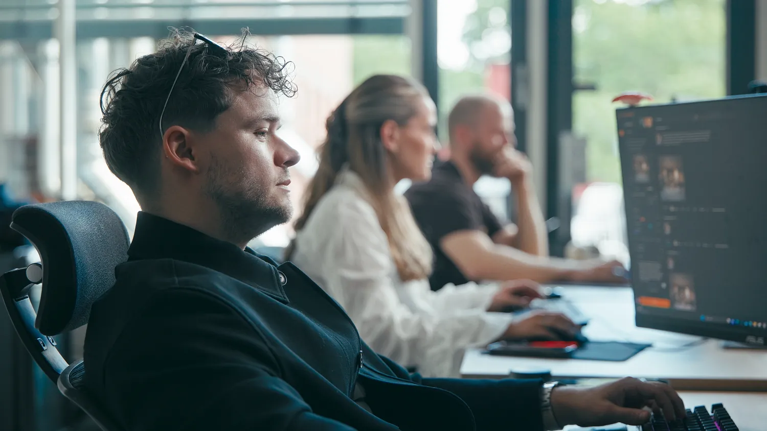 Three colleagues working along a desk row by the windows